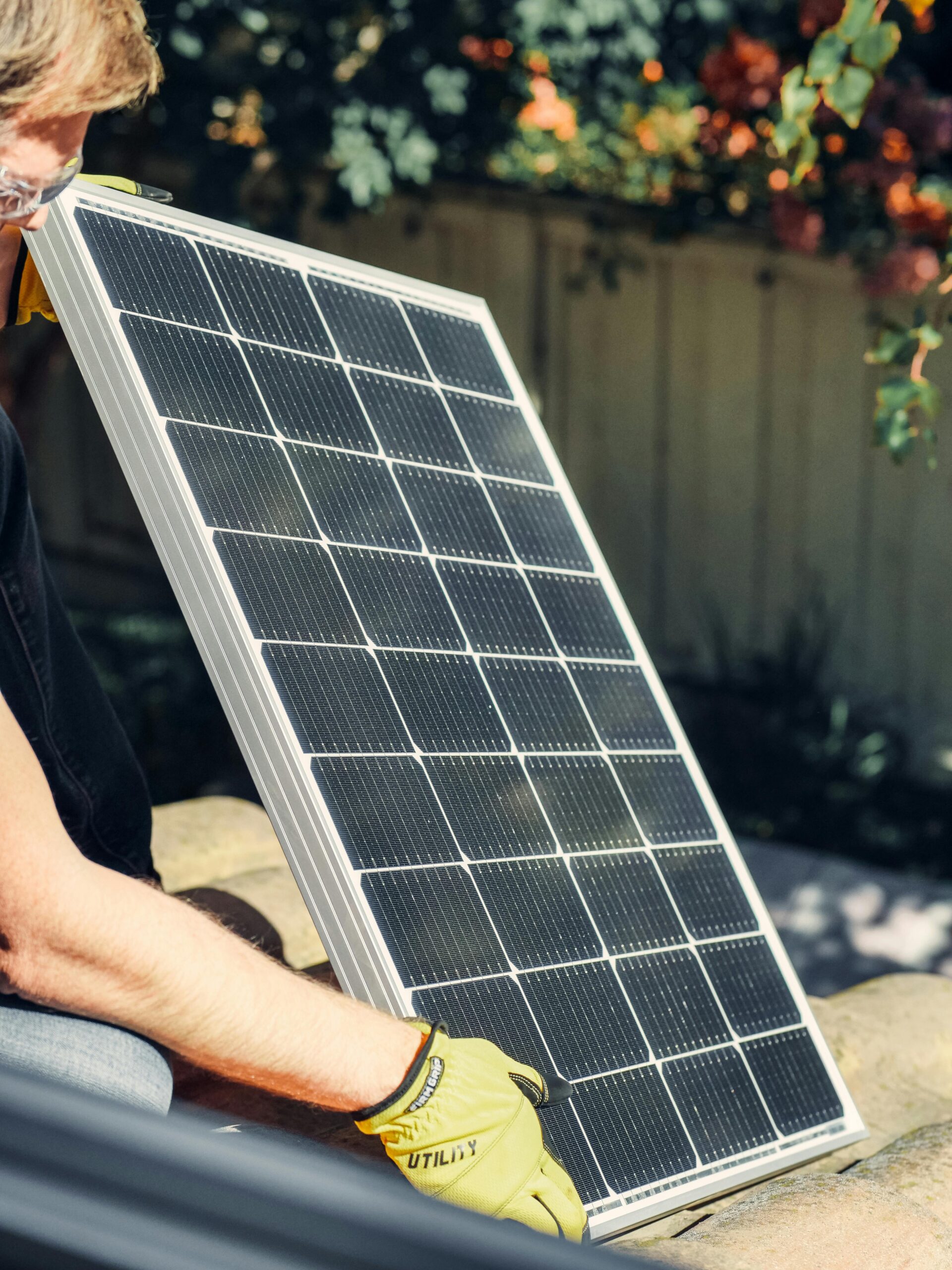 A worker installs a solar panel in a garden, promoting clean energy.